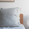 Natural European linen pillowcaseson a bed with a wooden headboard against a white wall