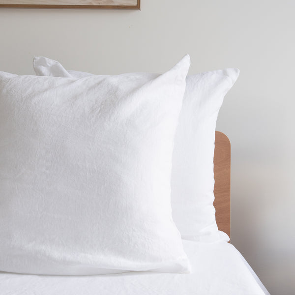 Pure white European linen pillowcases on a bed against a neutral wall