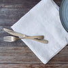 Silver knife and fork on a white linen napkin with a wooden surface