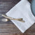 Silver knife and fork on a white linen napkin with a wooden surface