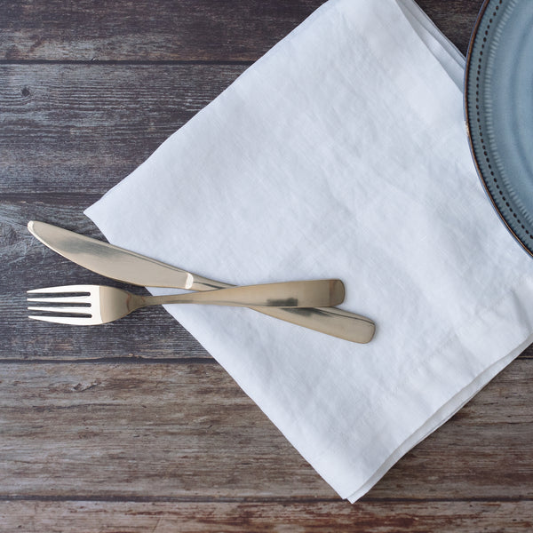 Silver knife and fork on a white linen napkin with a wooden surface