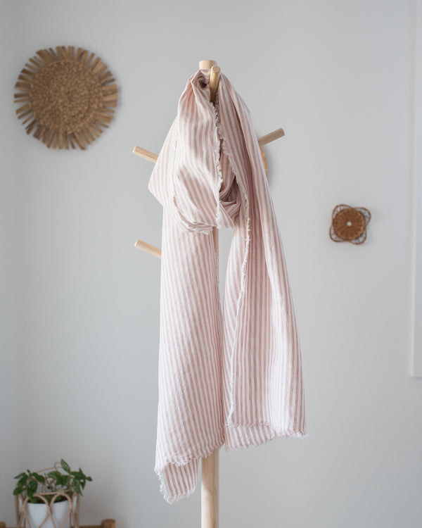 Pink striped scarf hanging on a wooden coat rack against a white wall.