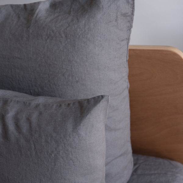 Charcoal grey European linen textured pillows on a bed with a wooden headboard.