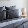 Greypillowcasesset on a bed with a lamp and side table in the background.