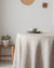 Round table with a beige tablecloth, green bowl, and white plate against a light gray wall.