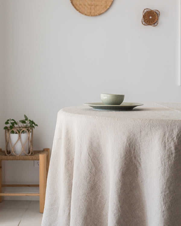 Round table with a beige tablecloth, green bowl, and white plate against a light gray wall.