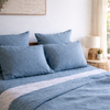 Lake blue linen pillowcases on a bed in a bright bedroom.