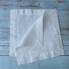 Pure White 100% Linen Cocktail Napkins on a blue wooden surface