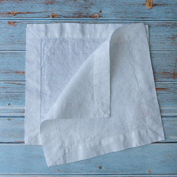 Pure White 100% Linen Cocktail Napkins on a blue wooden surface