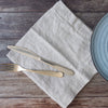 Silver knife and fork on a light natural napkin with a blue plate on a wooden surface