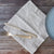 Silver knife and fork on a light natural napkin with a blue plate on a wooden surface