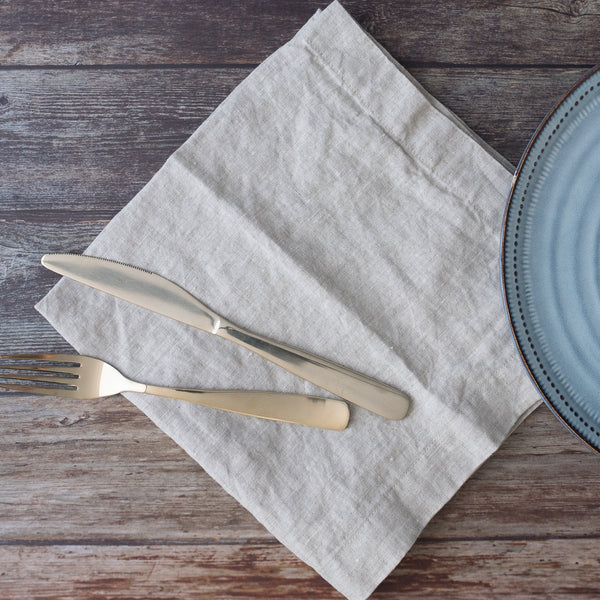 Silver knife and fork on a light natural napkin with a blue plate on a wooden surface