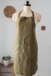 Green apron on a mannequin against a white wall with decorative elements.