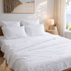 White bedding set on a bed in a bedroom with a lamp and decor.
