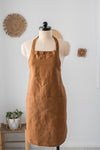 Brown apron on a mannequin against a white wall with decorative elements.